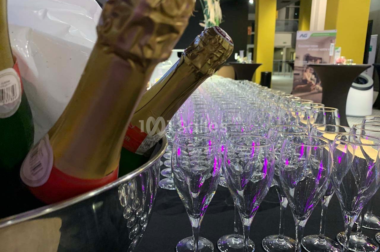 Bouteille de champagne dans un seau et rangée de flûtes vides alignées sur une table lors d'un événement.
