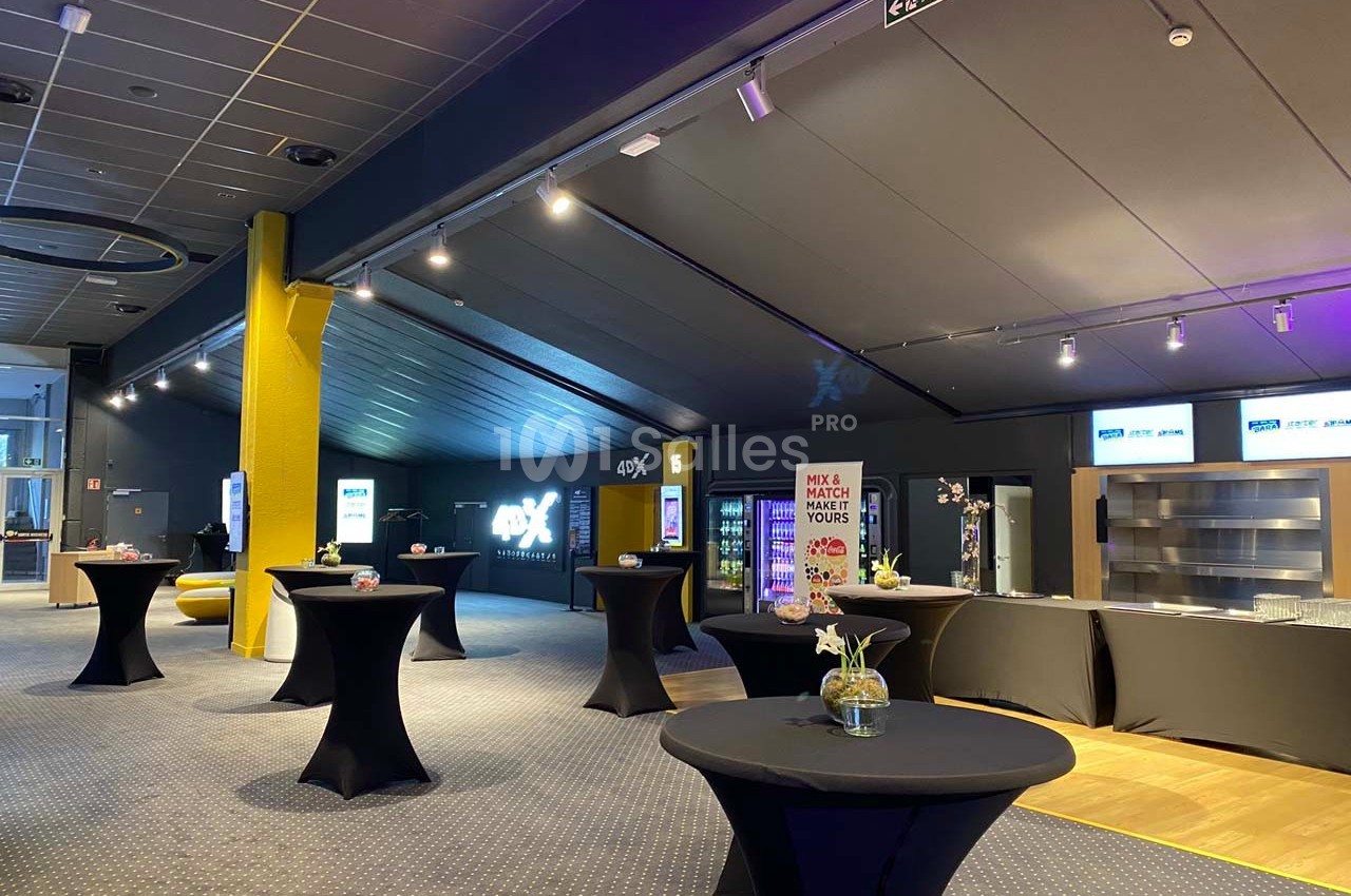 Salle d'événement avec tables hautes noires, comptoirs en arrière-plan et éclairage tamisé.