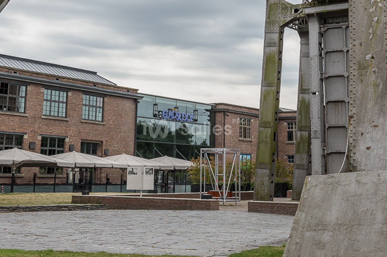 Bâtiments en briques avec grandes fenêtres, terrasse avec parasols et structure métallique au premier plan.