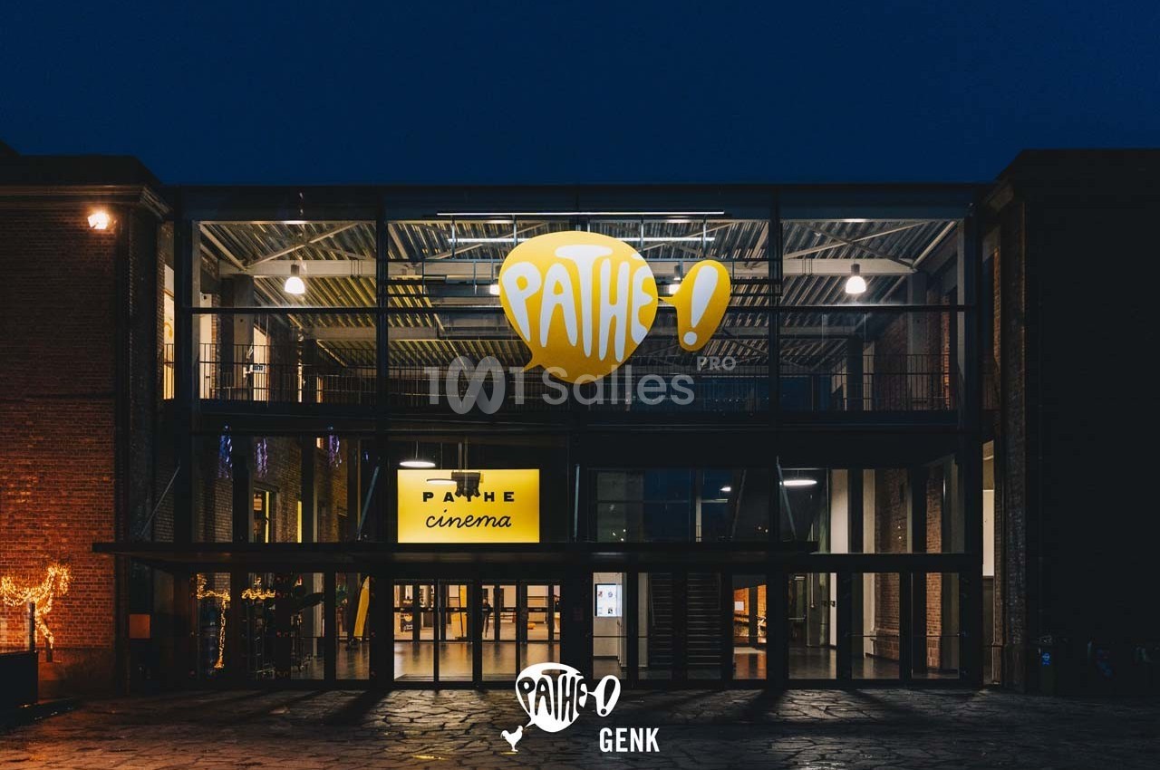 Façade vitrée d'un cinéma Pathé illuminé de nuit, avec le logo jaune visible au-dessus de l'entrée principale.