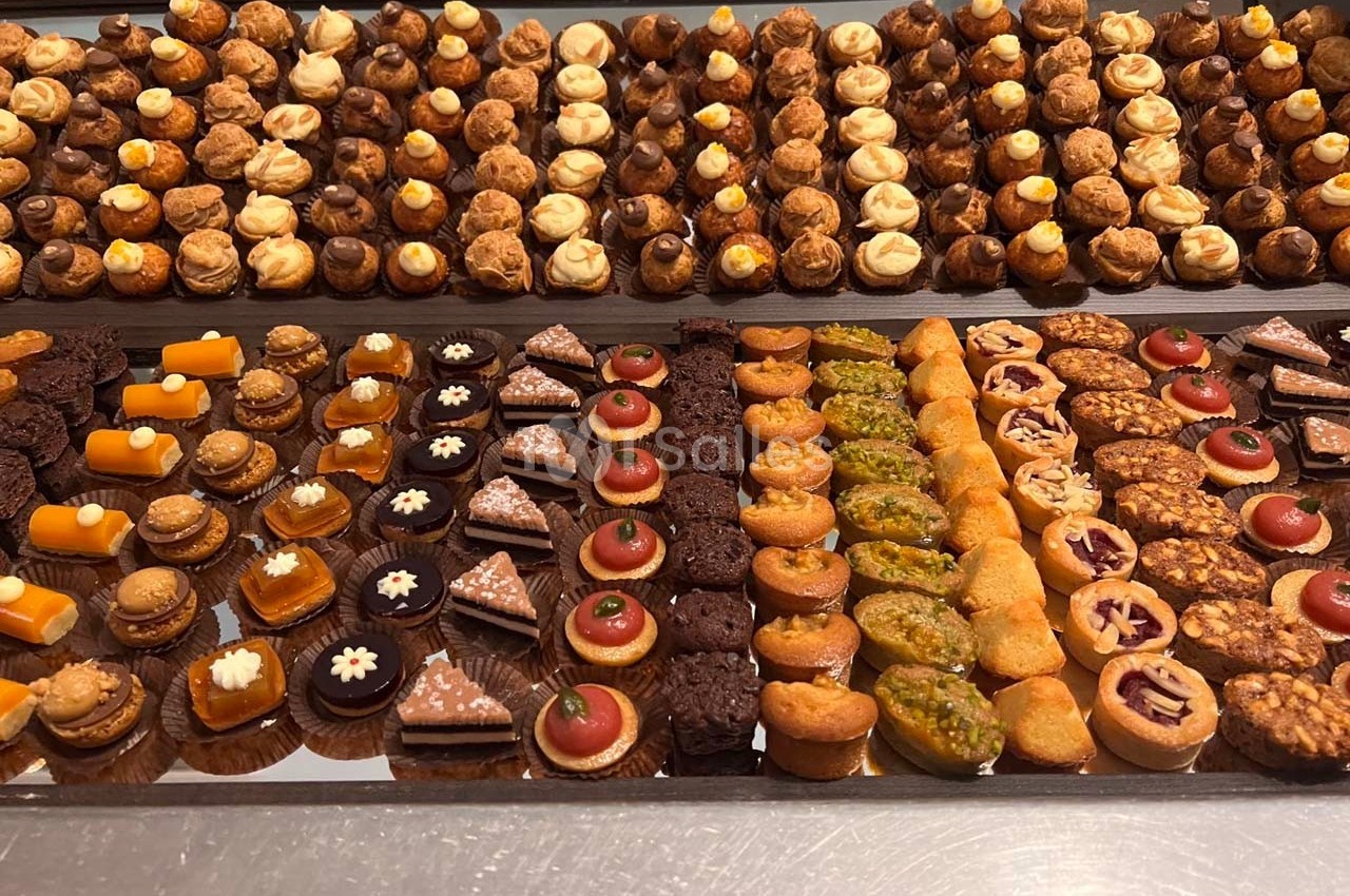 Plateau de pâtisseries variées disposées en rangées, comprenant éclairs, tartelettes, gâteaux et autres desserts miniatures.