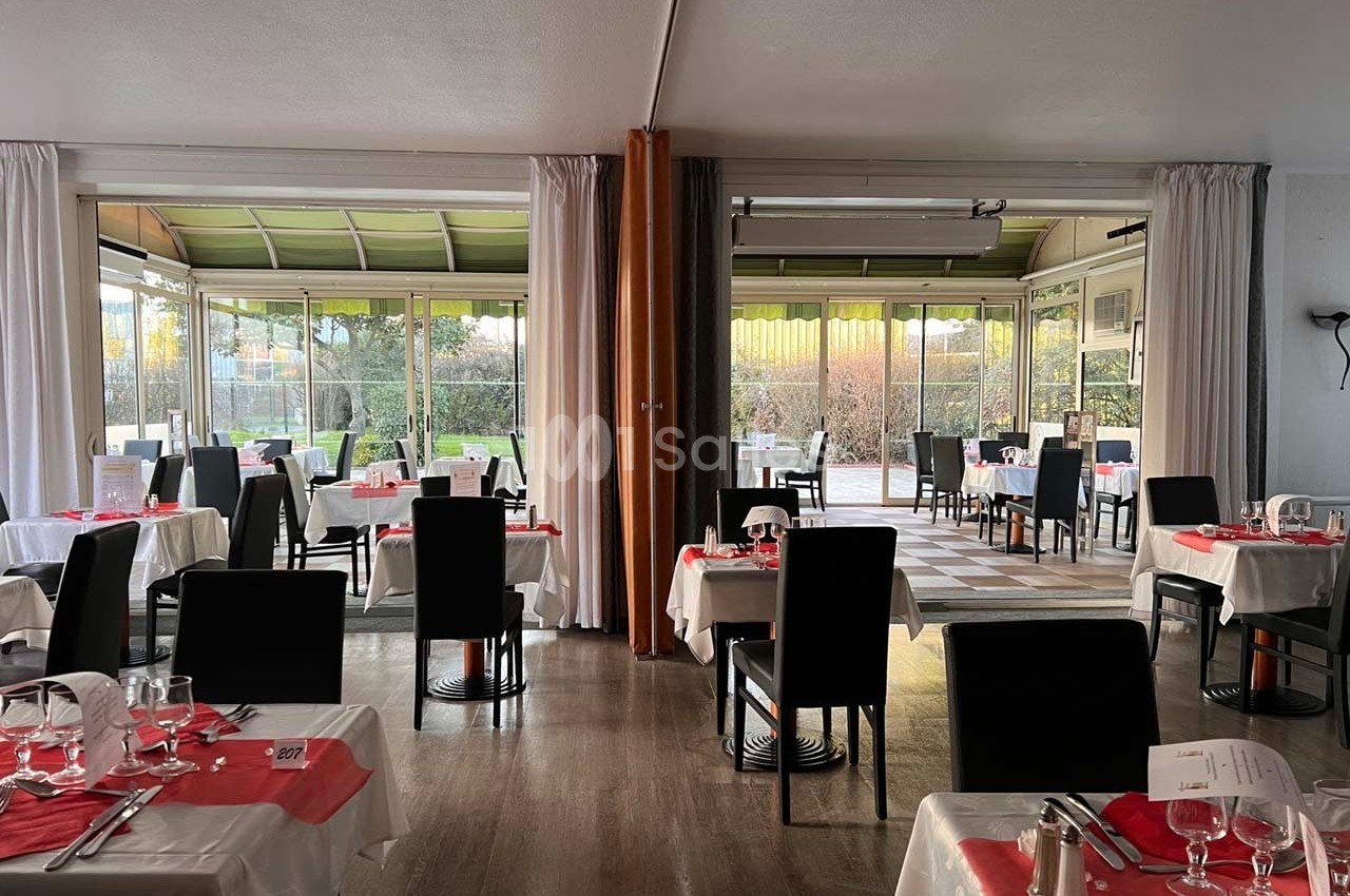 Salle de restaurant lumineuse avec tables dressées, nappes blanches et rouges, et grandes baies vitrées donnant sur l…
