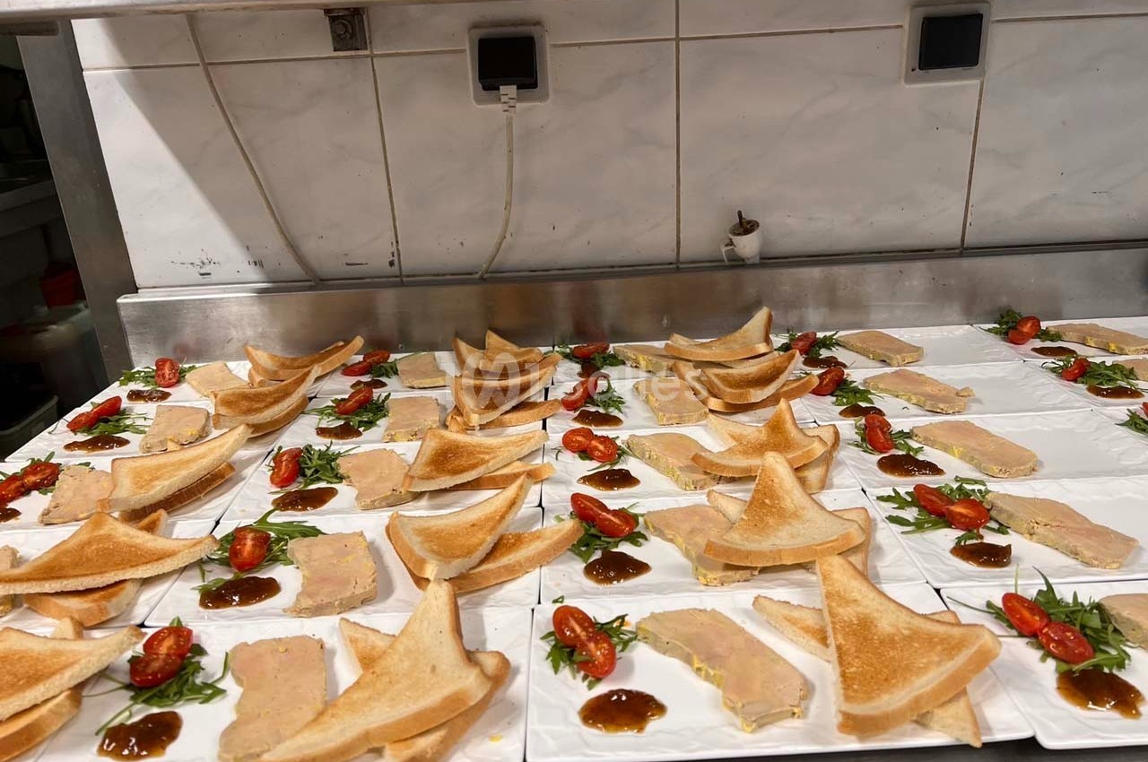 Assiettes dressées avec des tranches de foie gras, toasts triangulaires, tomates cerises et sauce sur un plan de travail.