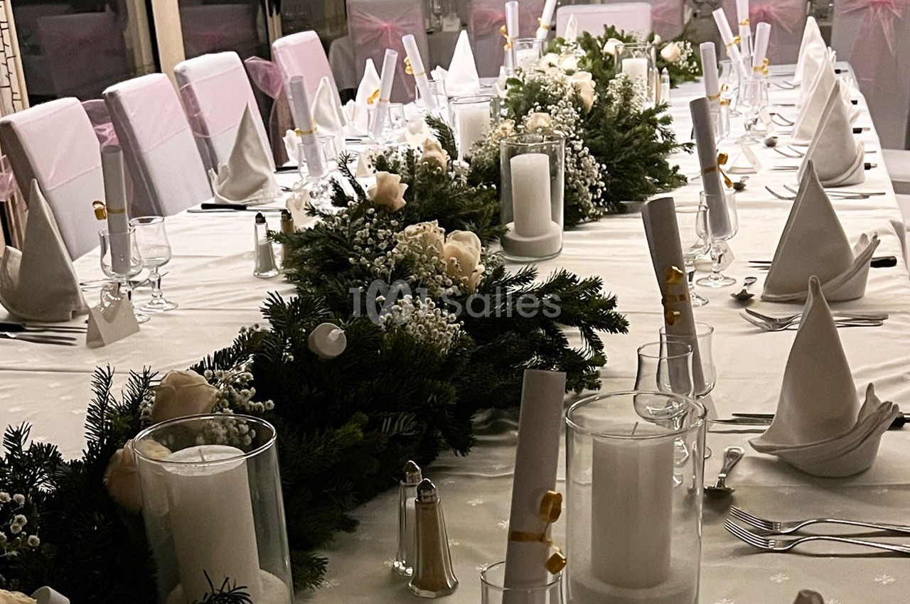 Table élégamment dressée avec nappes blanches, serviettes pliées, bougies et décorations florales.