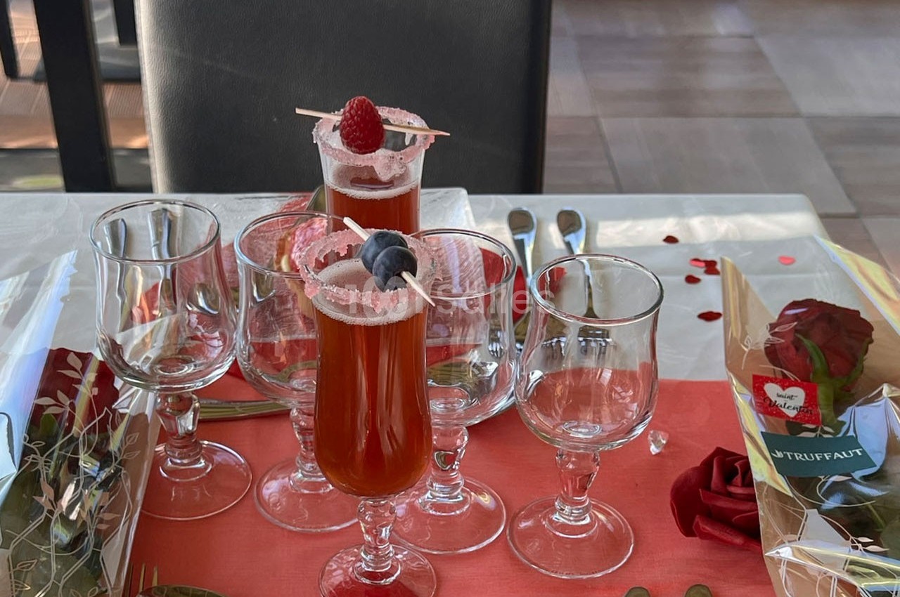 Verres de cocktail rouge décorés de fruits, entourés de verres à pied vides sur une table dressée avec une rose.