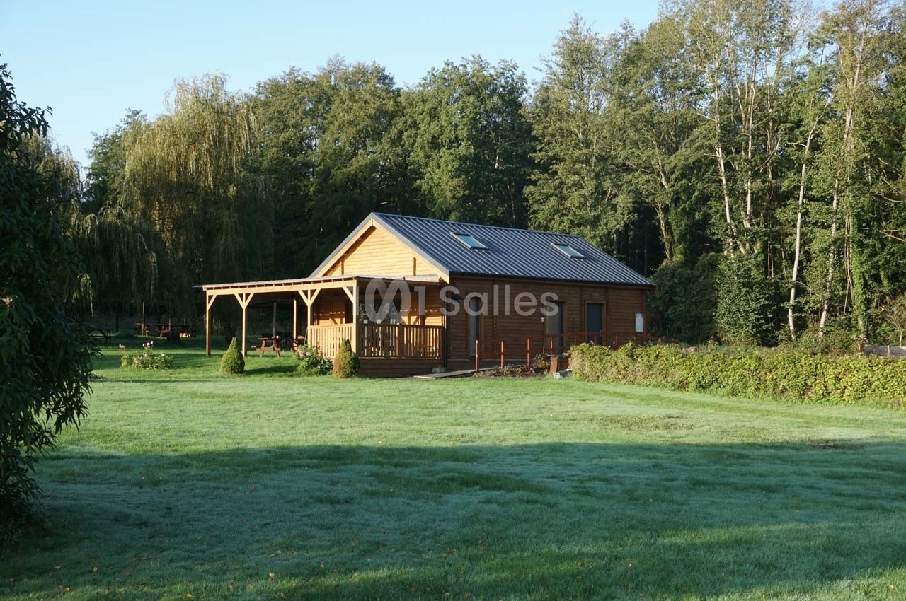 Chalet en bois avec terrasse, entouré de pelouse et bordé d'arbres dans un cadre naturel.