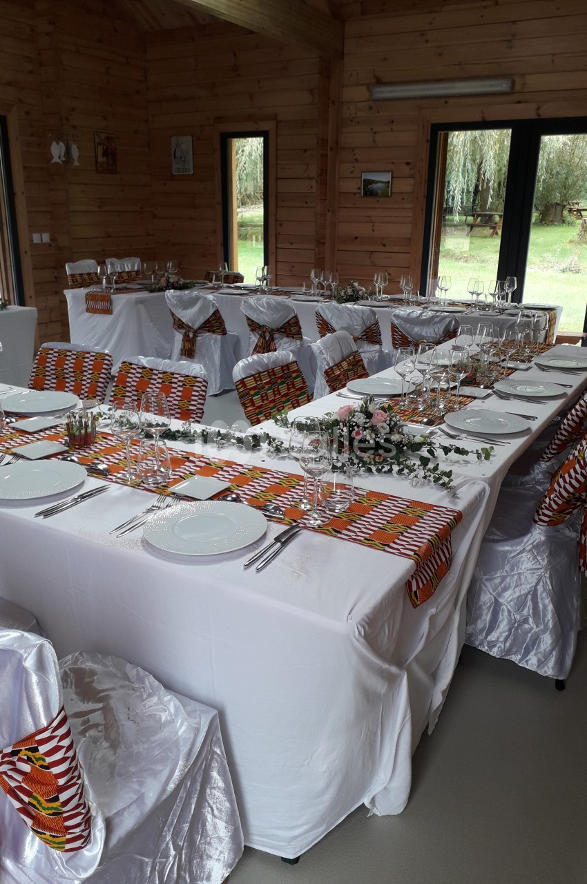 Salle décorée pour un repas festif, avec tables dressées, nappes blanches et touches de tissu coloré.