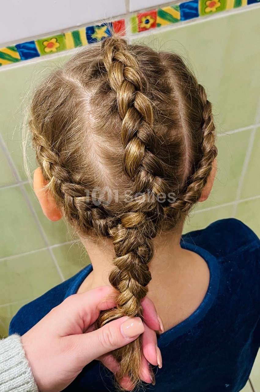 Vue de dos d'une enfant avec des tresses serrées et symétriques, tenue par une main.