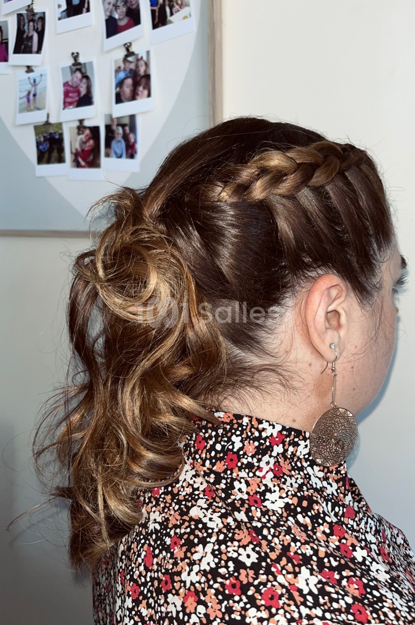 Femme de dos avec une coiffure tressée et attachée, portant une blouse fleurie et des boucles d'oreilles pendantes.
