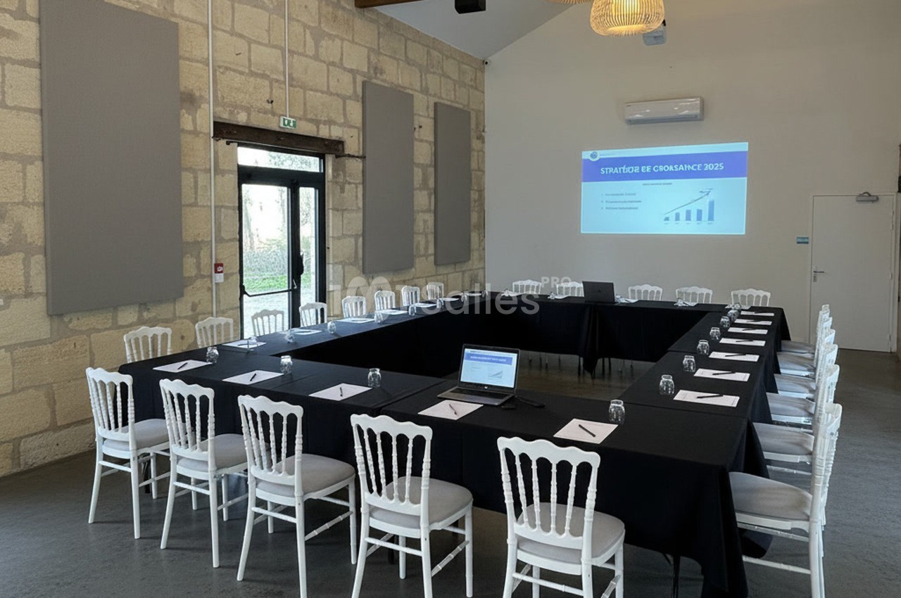 Salle de réunion lumineuse avec tables en U, chaises blanches et écran projetant une présentation.