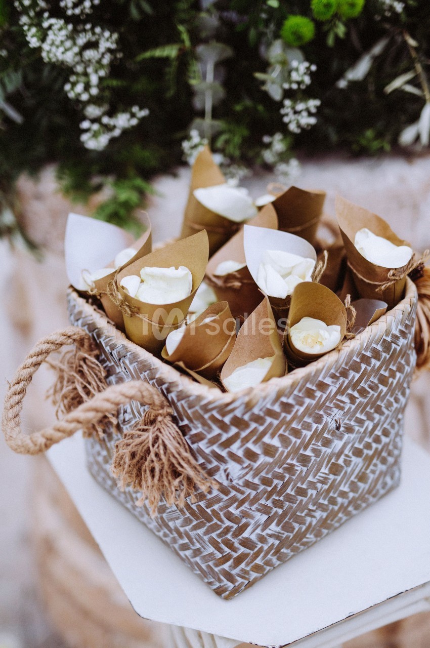 Cônes en papier kraft remplis de pétales blancs disposés dans un panier tressé avec des poignées en corde.