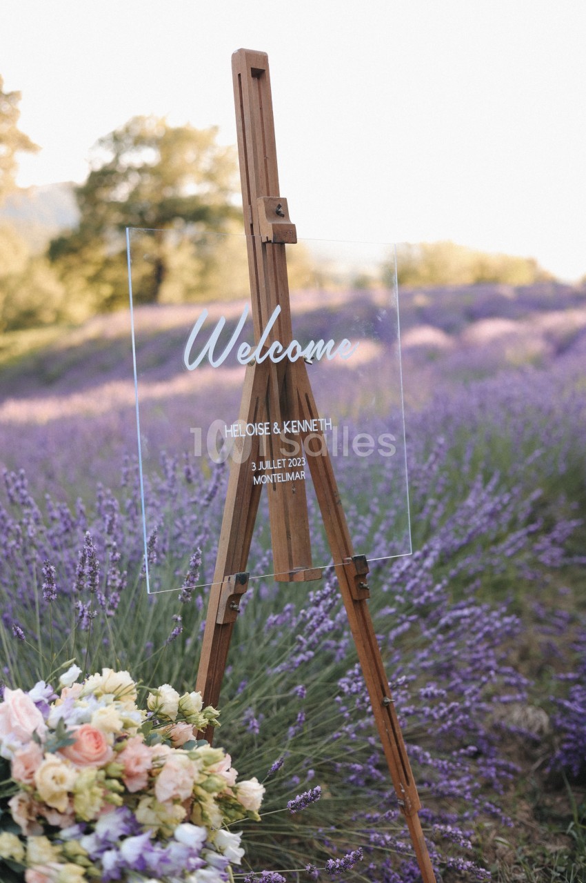 Chevalet en bois avec un panneau transparent indiquant un message de bienvenue, placé dans un champ de lavande.