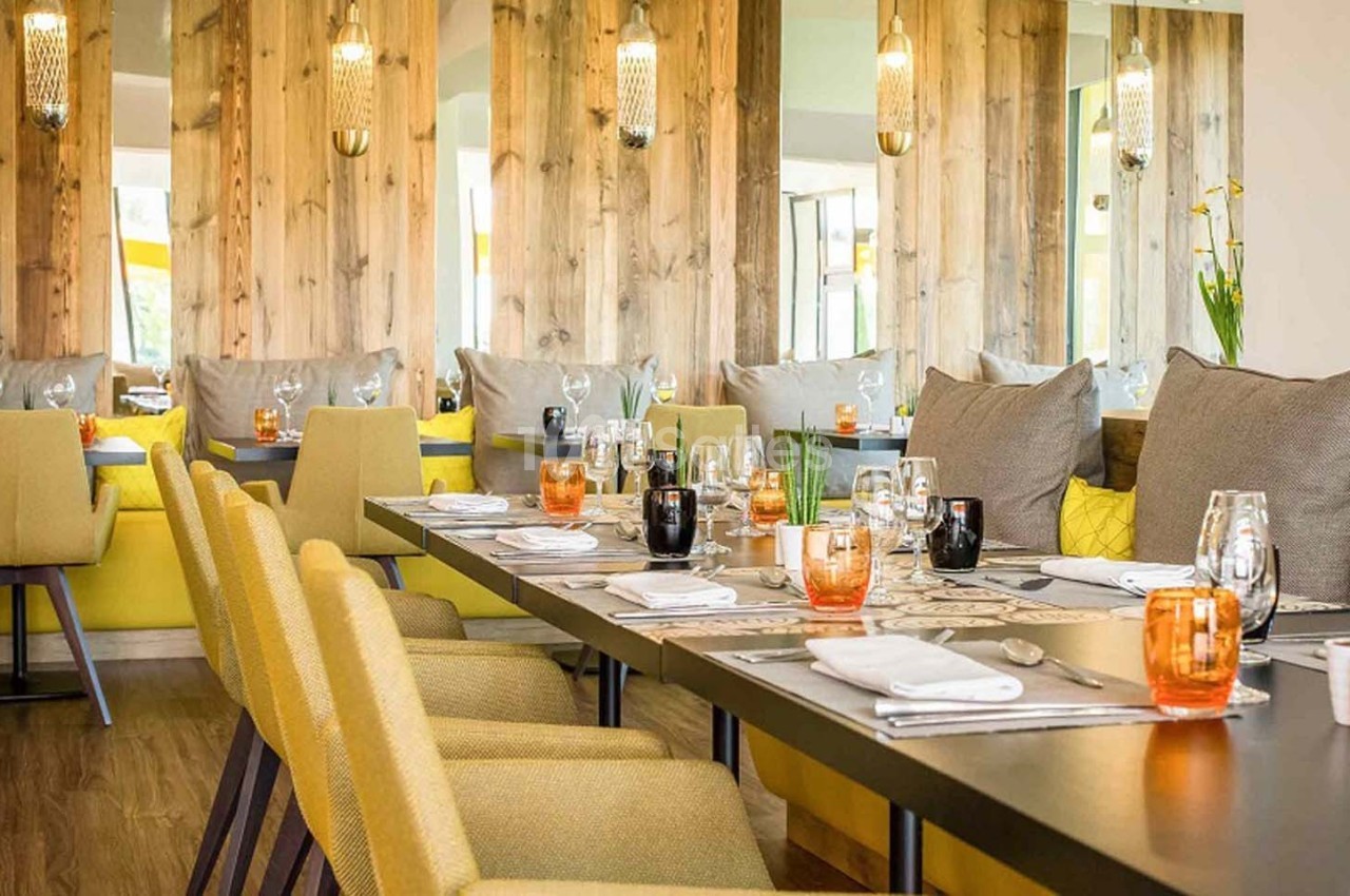 Salle de restaurant lumineuse avec tables dressées, chaises jaunes, murs en bois et miroirs décoratifs.
