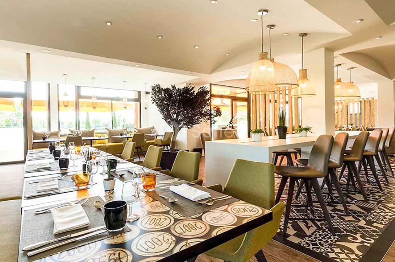 Salle de restaurant lumineuse avec tables dressées, chaises modernes et suspensions en osier.