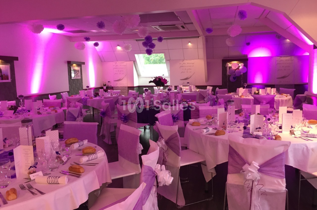 Salle de réception décorée en violet et blanc avec tables dressées pour un événement festif.