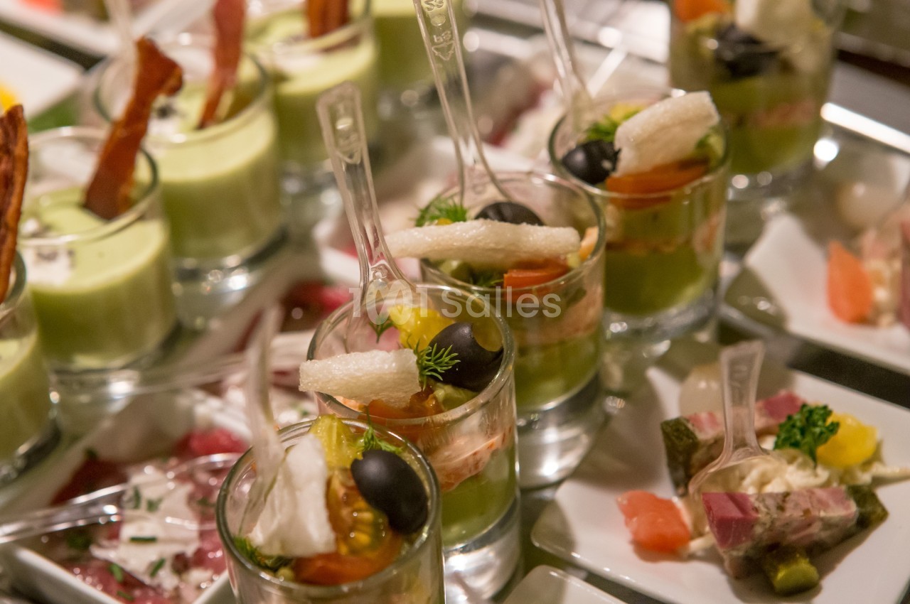 Verrines variées avec légumes, olives, et garnitures, présentées sur un plateau lors d'un buffet.