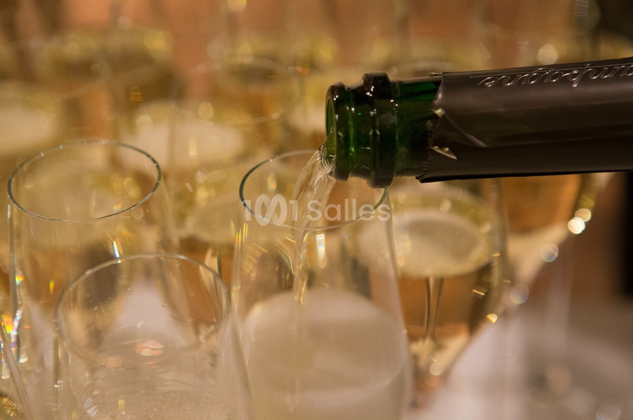 Un verre de champagne est rempli depuis une bouteille, entouré de flûtes déjà servies.