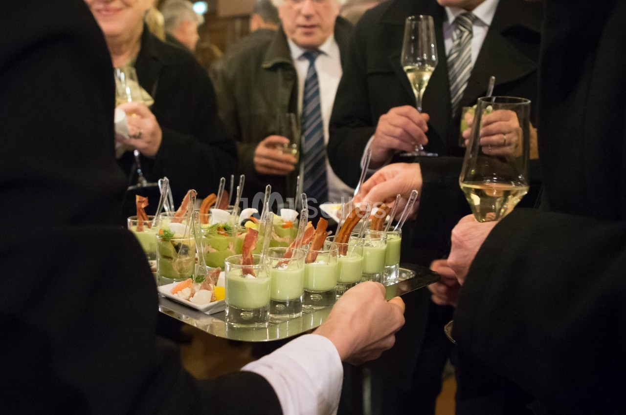 Personnes debout dégustant des verrines et des amuse-bouches lors d'un événement avec des verres de vin à la main.