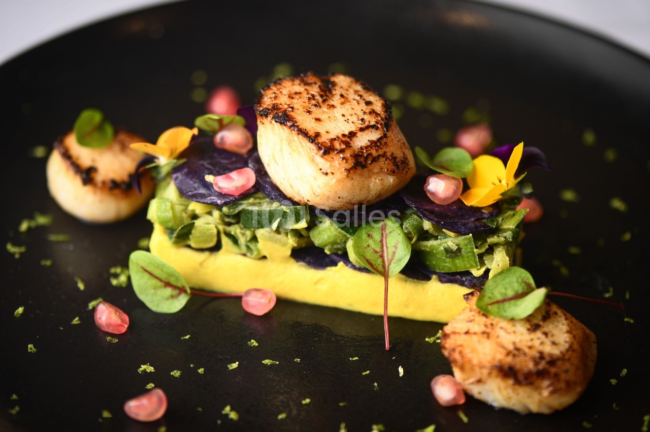 Assiette gastronomique avec noix de Saint-Jacques poêlées, purée, légumes verts, pommes grenades et fleurs comestibles.