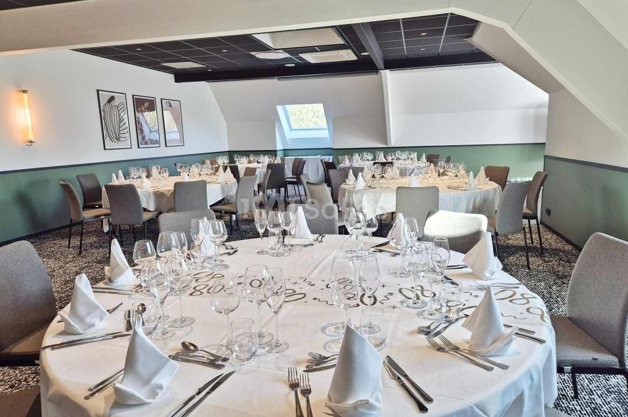Salle de réception lumineuse avec tables rondes dressées, nappes blanches et chaises grises.
