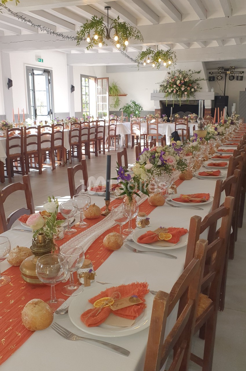 Salle de réception décorée avec des tables dressées, nappes blanches, fleurs et assiettes garnies de saumon fumé.