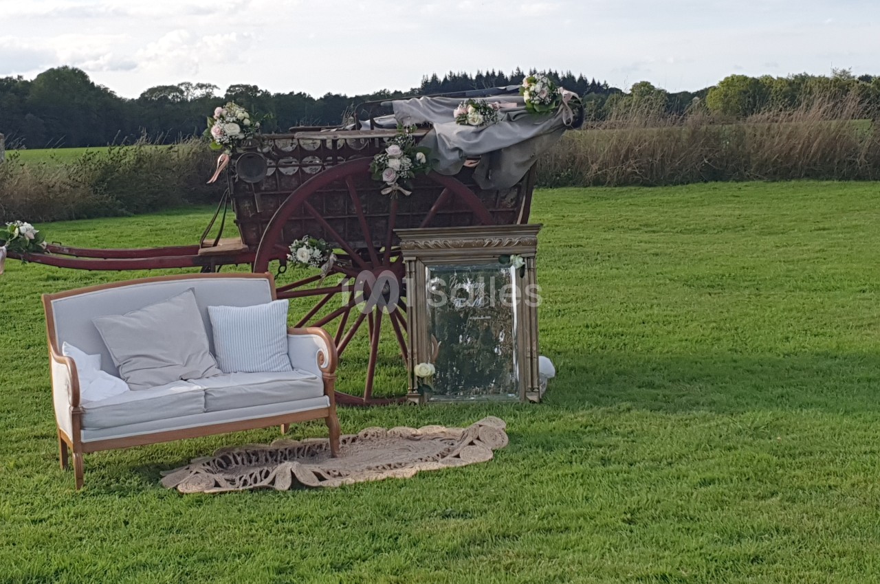 Charrette décorée de fleurs, canapé blanc et miroir posés sur une pelouse en plein air.