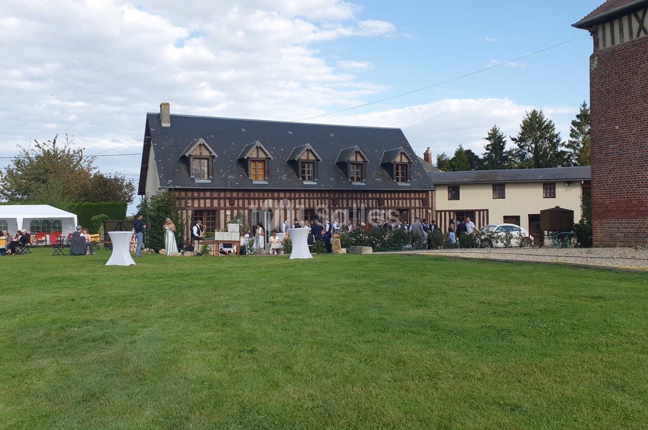 Grande maison à colombages avec jardin, tables hautes et invités rassemblés pour un événement en plein air.