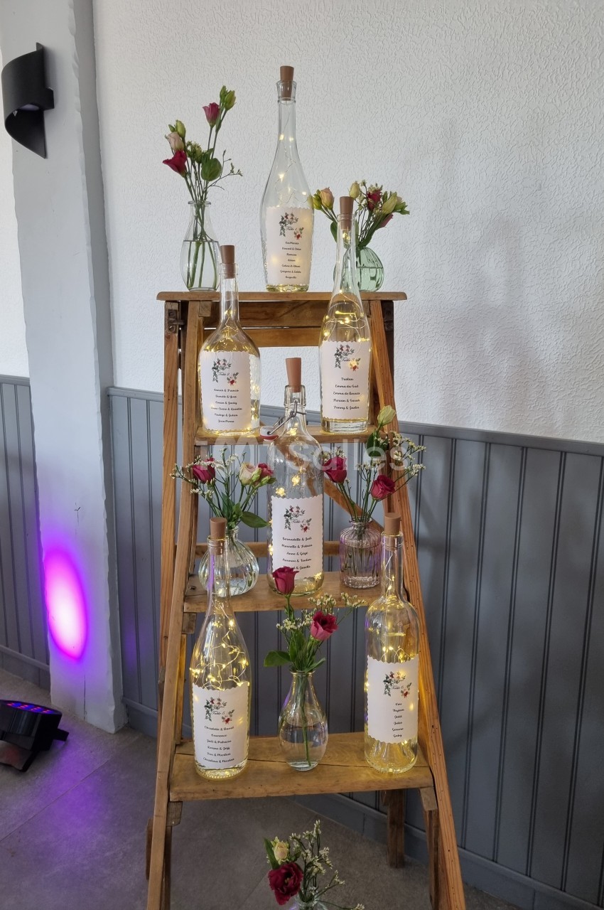 Échelle en bois décorée de bouteilles lumineuses et de petits bouquets de fleurs rouges et jaunes.