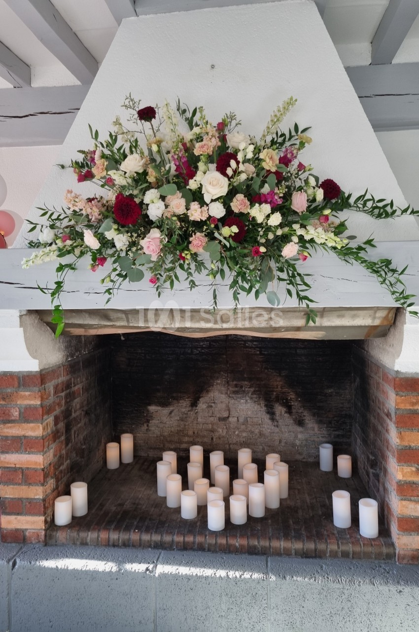 Cheminée en briques décorée de fleurs colorées et de bougies blanches disposées à l'intérieur.