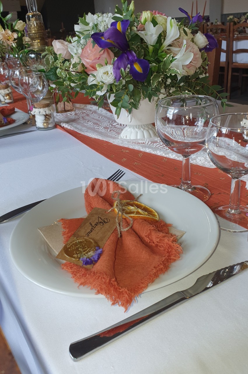 Table dressée avec une assiette blanche, une serviette orange décorée d'un brin de lavande et un centre de table fleuri.