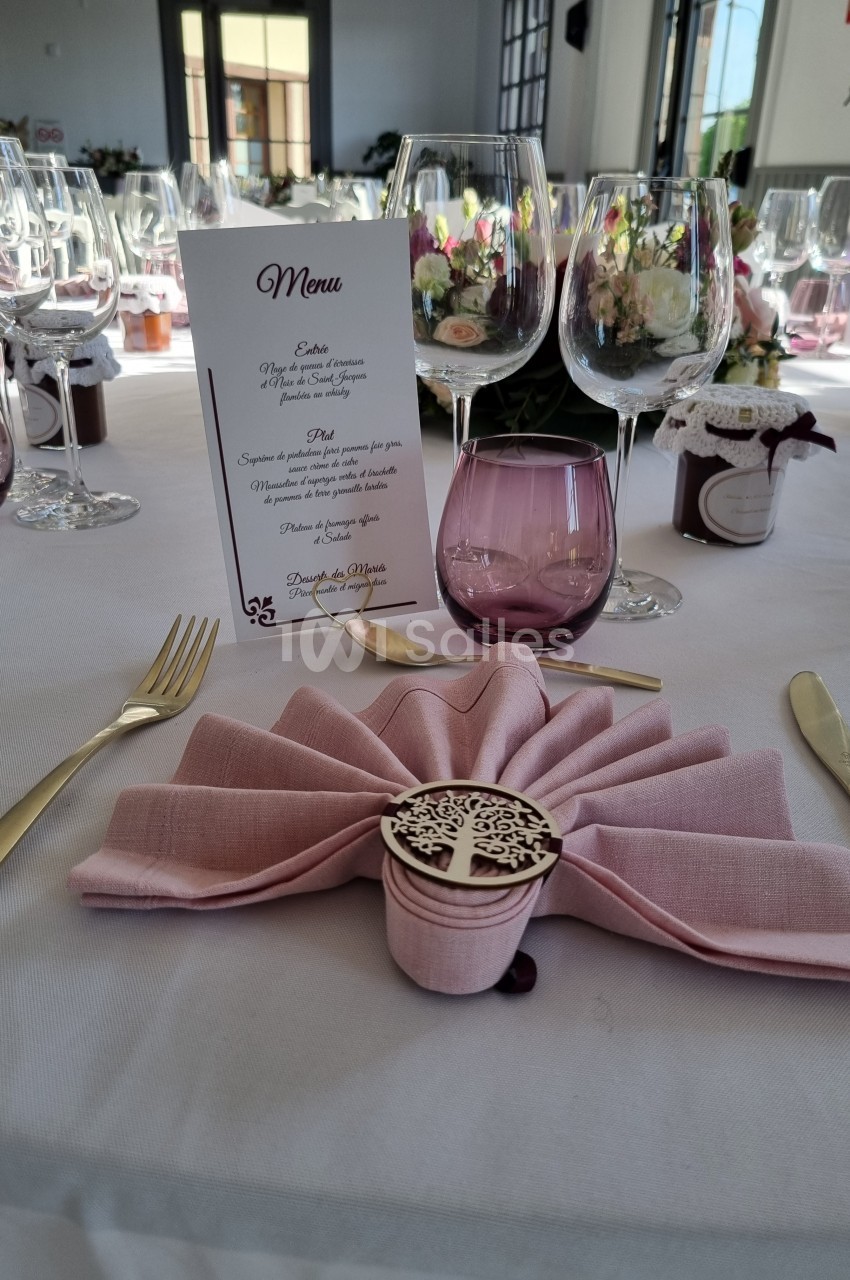 Table de réception élégamment dressée avec serviette pliée, menu, verres et décorations florales.