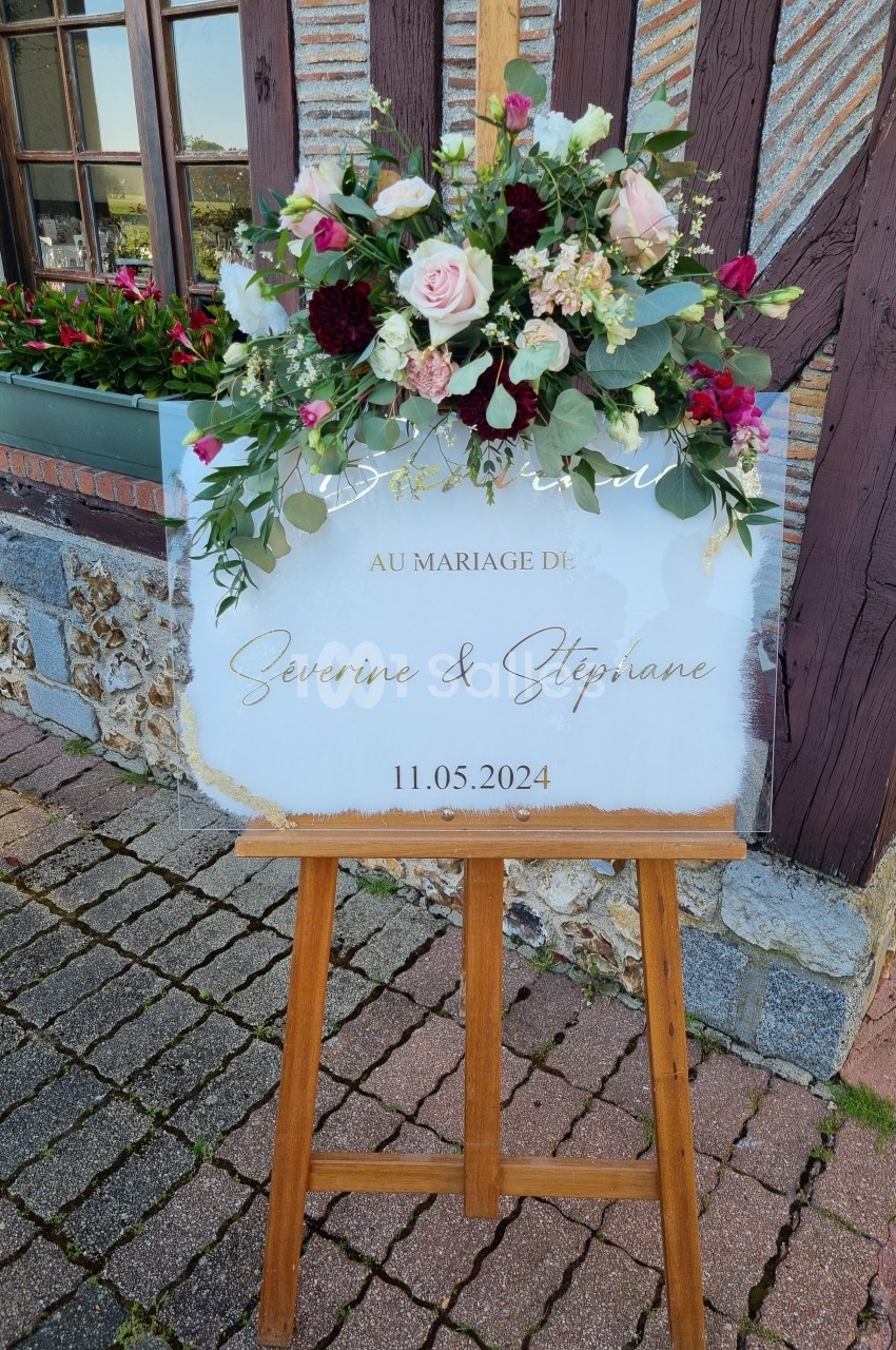 Panneau de mariage sur chevalet en bois, décoré de fleurs colorées, avec les prénoms des mariés et la date du 11 mai 2024.
