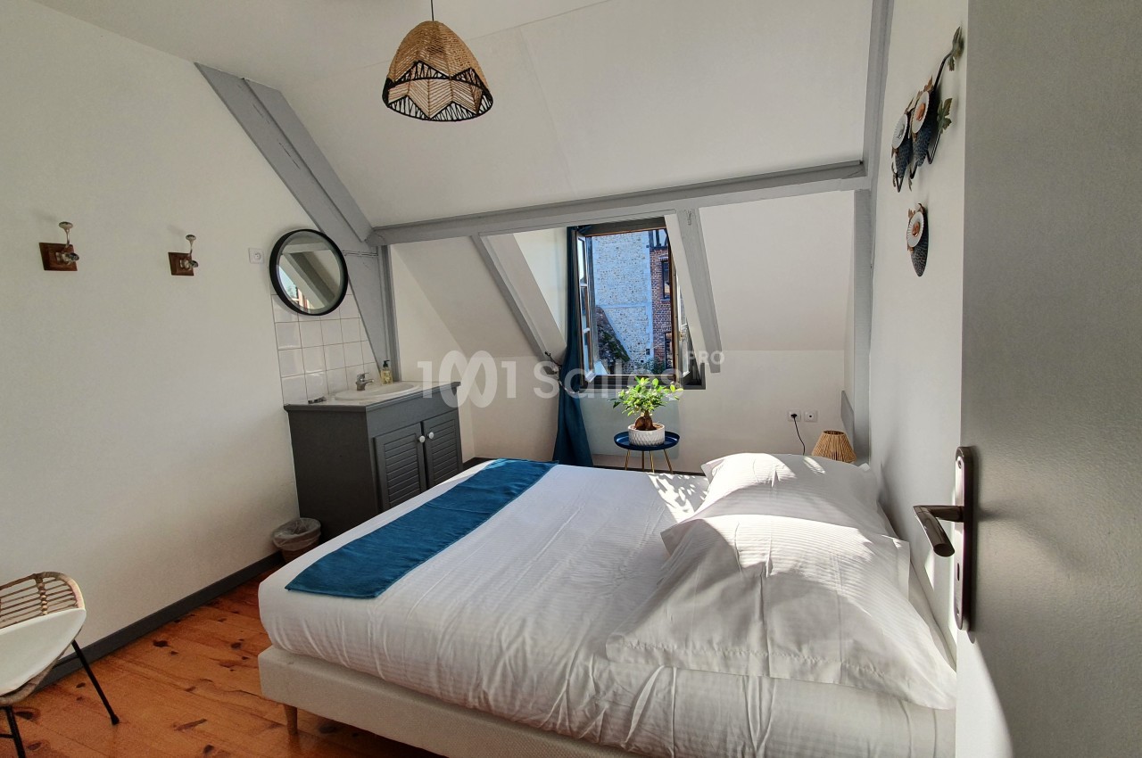 Chambre lumineuse sous combles avec lit double, fenêtre ouverte, mobilier minimaliste et décoration sobre.