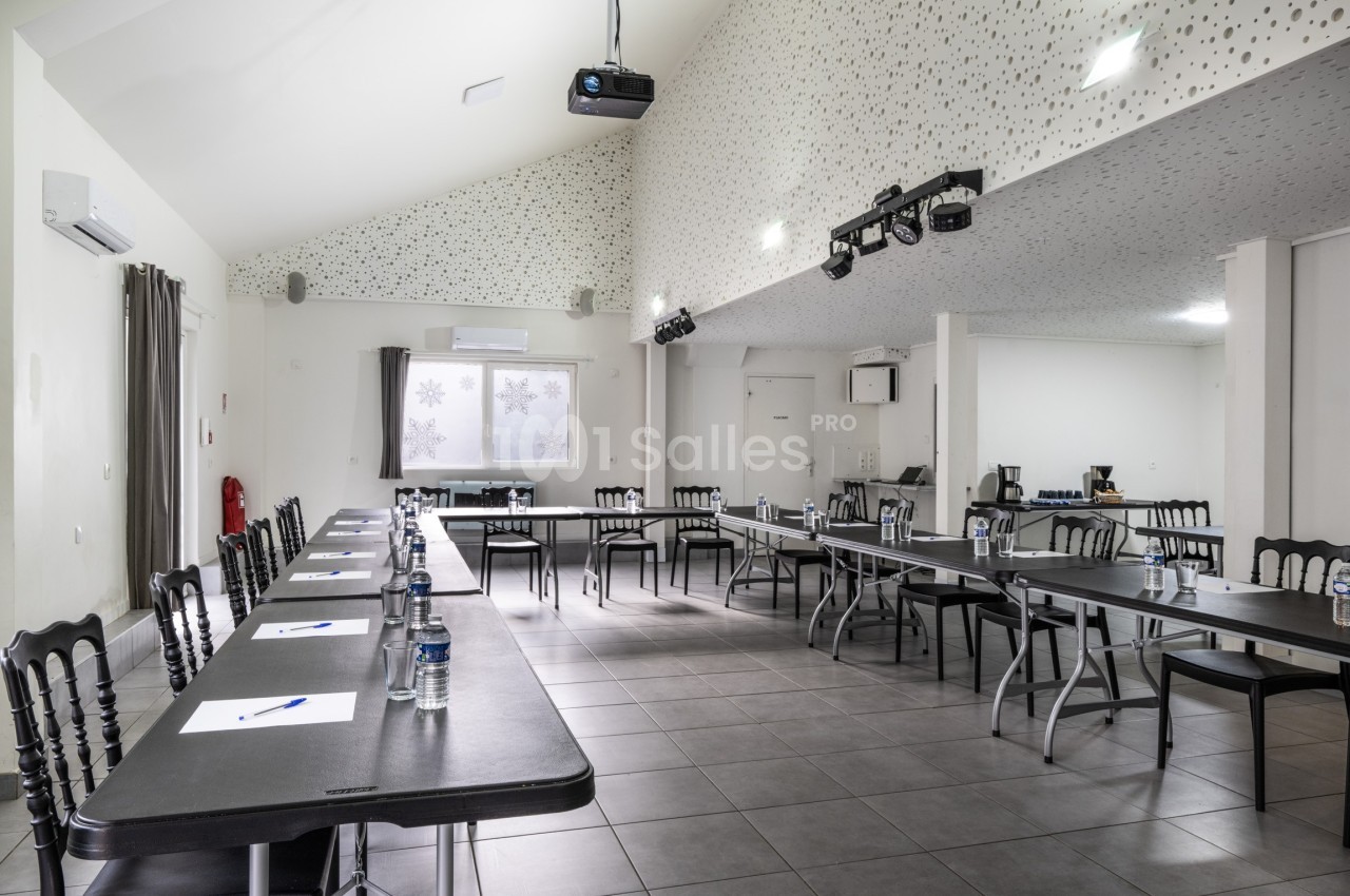 Salle de réunion lumineuse avec tables disposées en U, chaises noires, bouteilles d'eau et matériel de présentation.