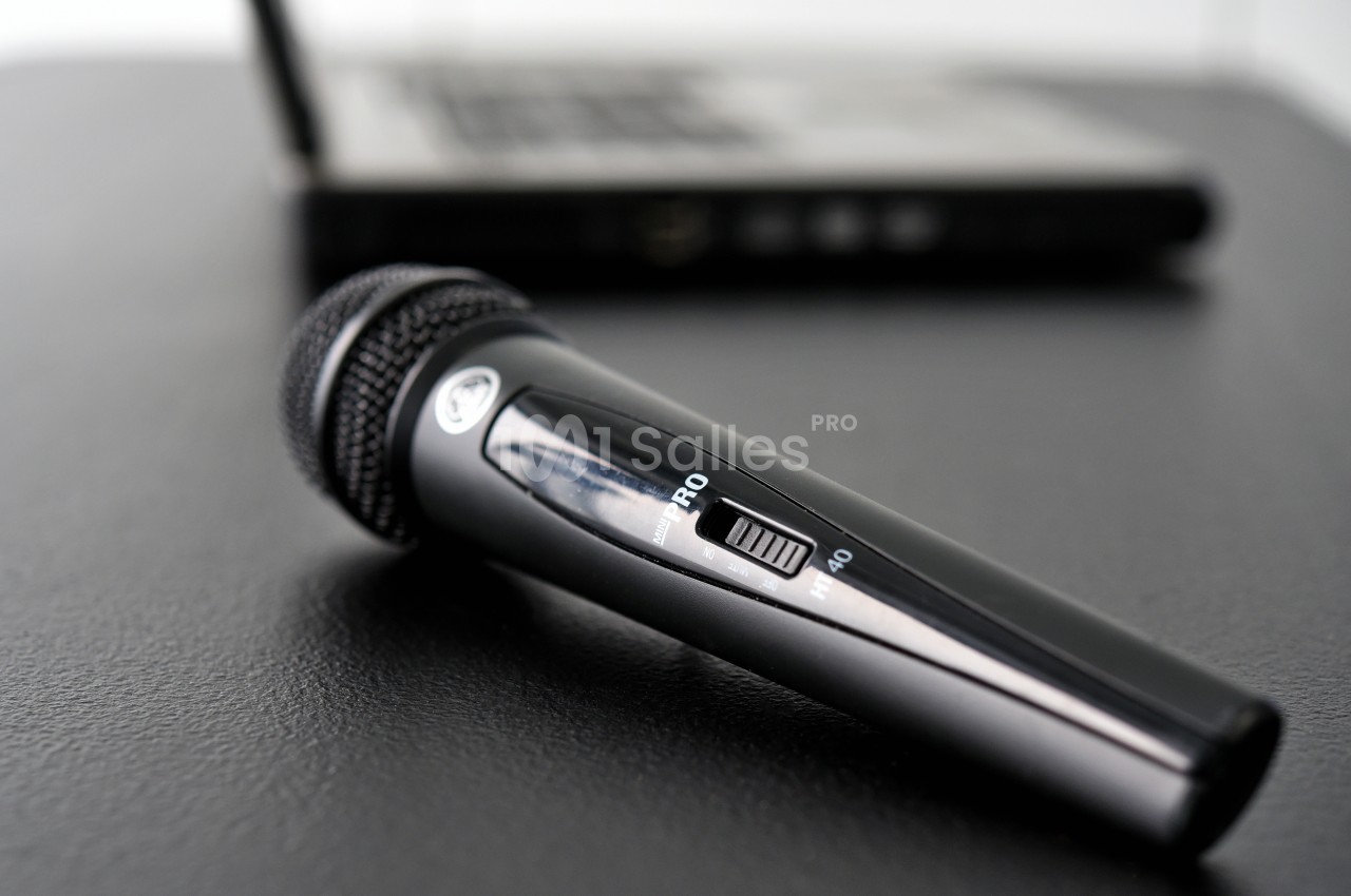 Microphone noir posé sur une table noire, avec un ordinateur portable flou en arrière-plan.