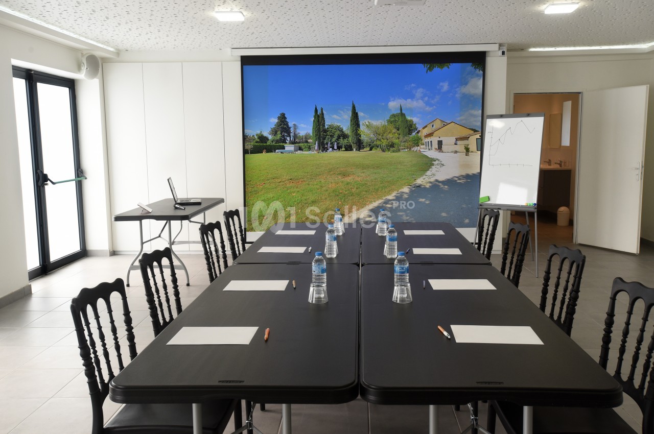 Salle de réunion lumineuse avec une grande table, des chaises, des documents, et un écran affichant un paysage extérieur.