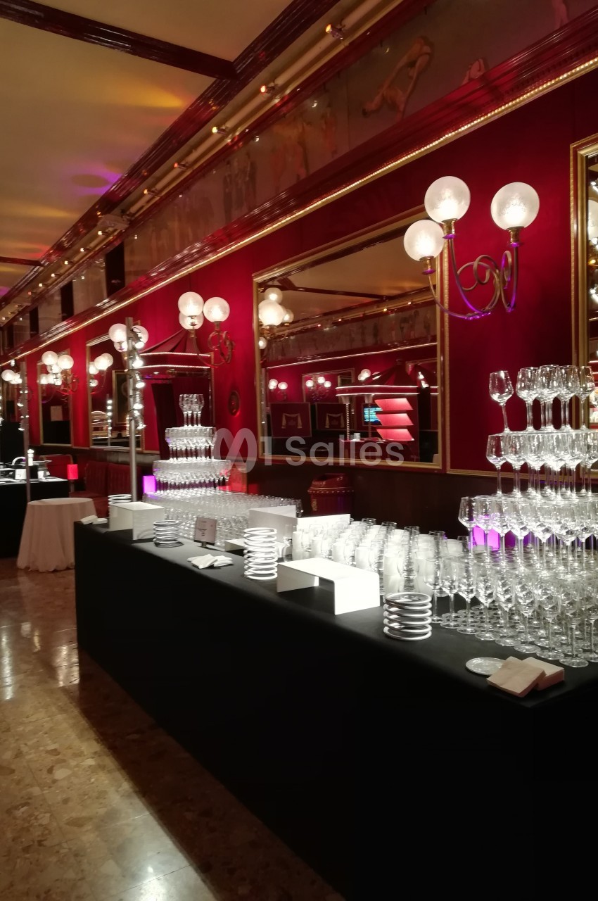 Salle élégante avec tables noires garnies de verres en cristal, éclairage chaleureux et décorations rouges et dorées.