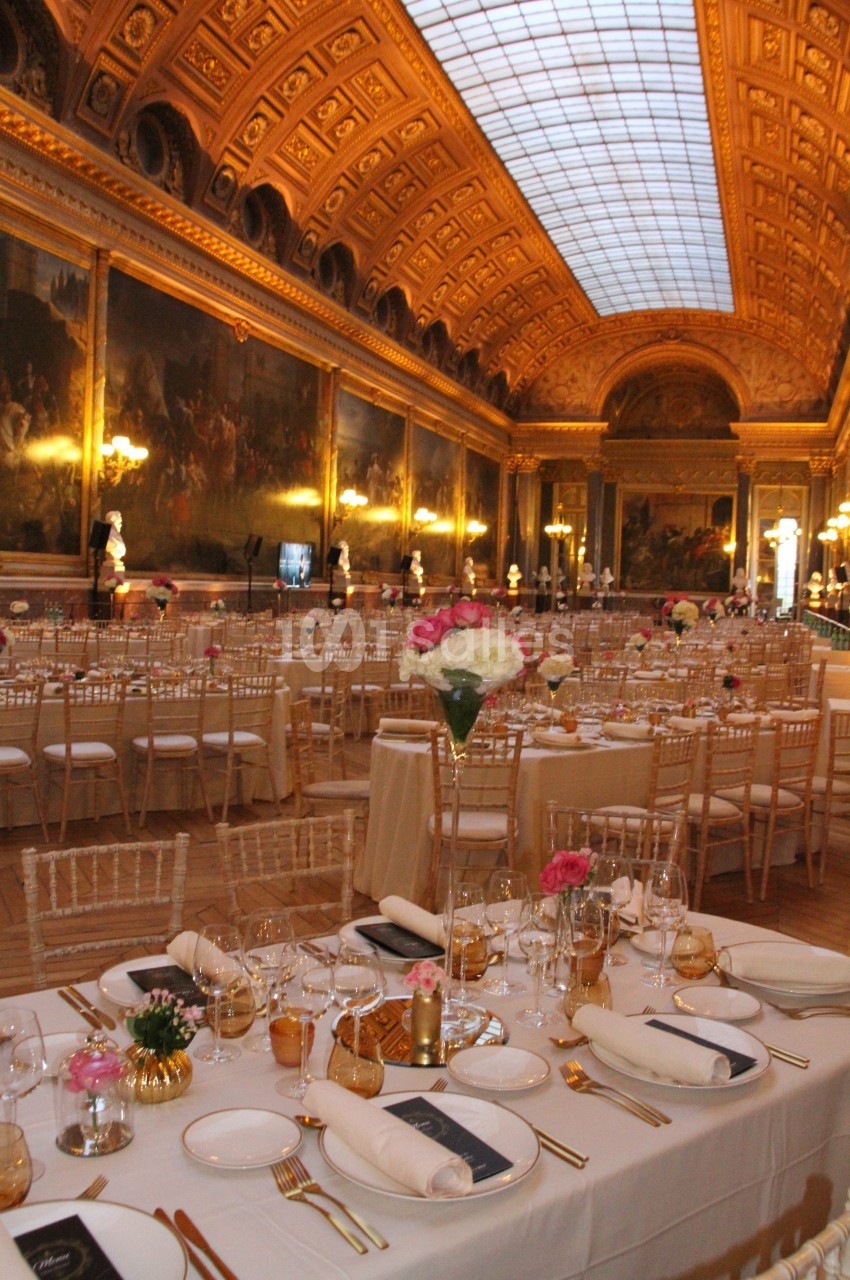 Salle ornée de peintures et de dorures, aménagée avec des tables élégantes pour un événement ou un dîner.