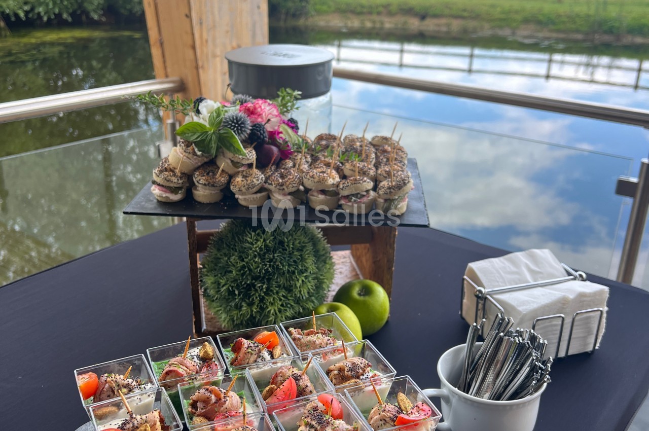 Plateau de bouchées apéritives et verrines colorées disposées sur une table près d'un plan d'eau.