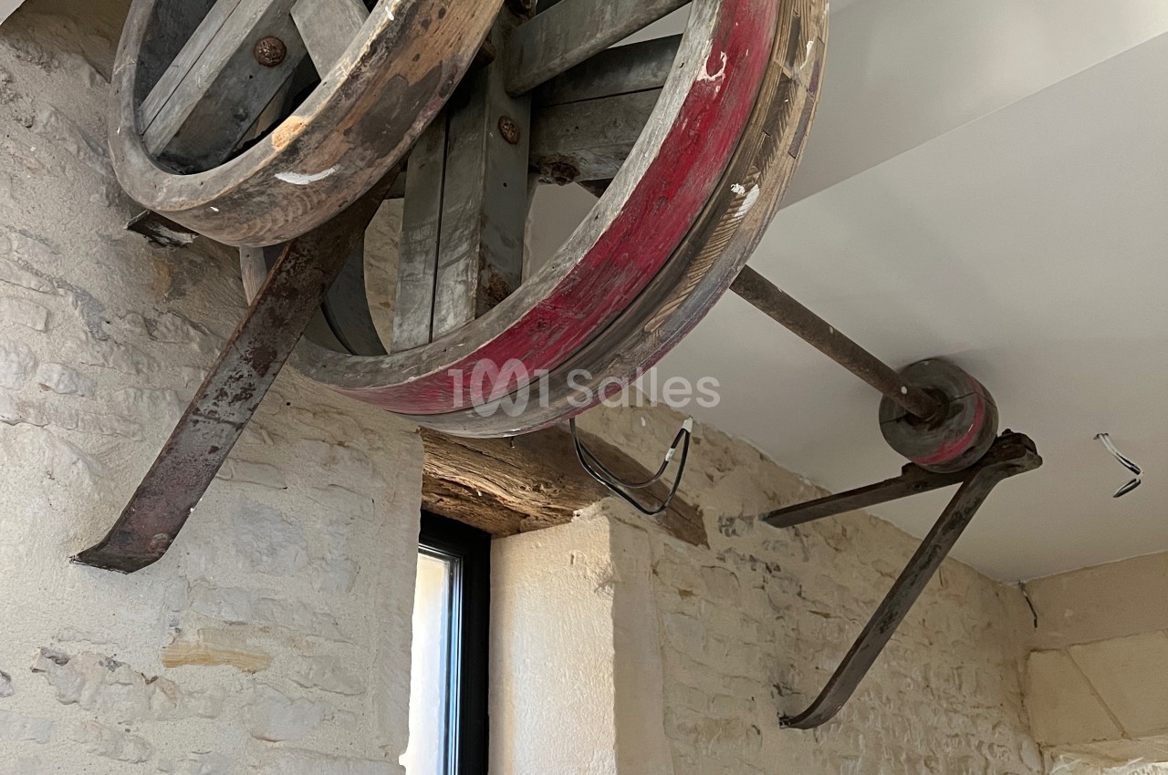 Mécanisme ancien avec roues en bois et métal fixé à un mur en pierre dans un intérieur lumineux.