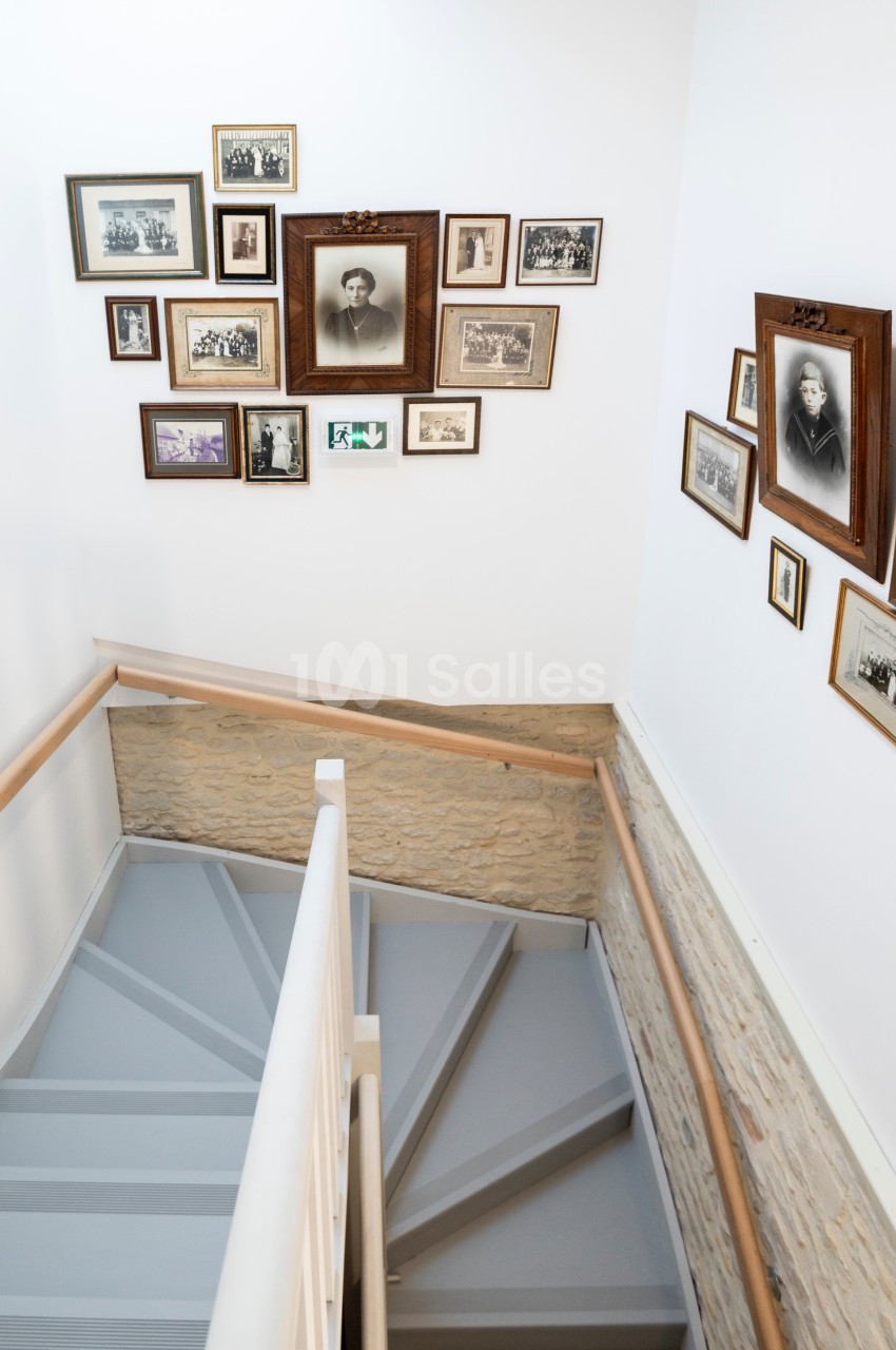 Escalier intérieur en bois peint en gris, entouré de murs ornés de cadres photo anciens.