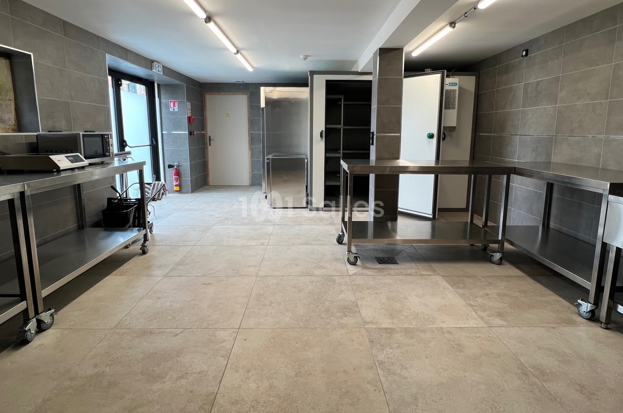 Cuisine professionnelle avec plans de travail en acier inoxydable, sol carrelé et équipements de stockage.