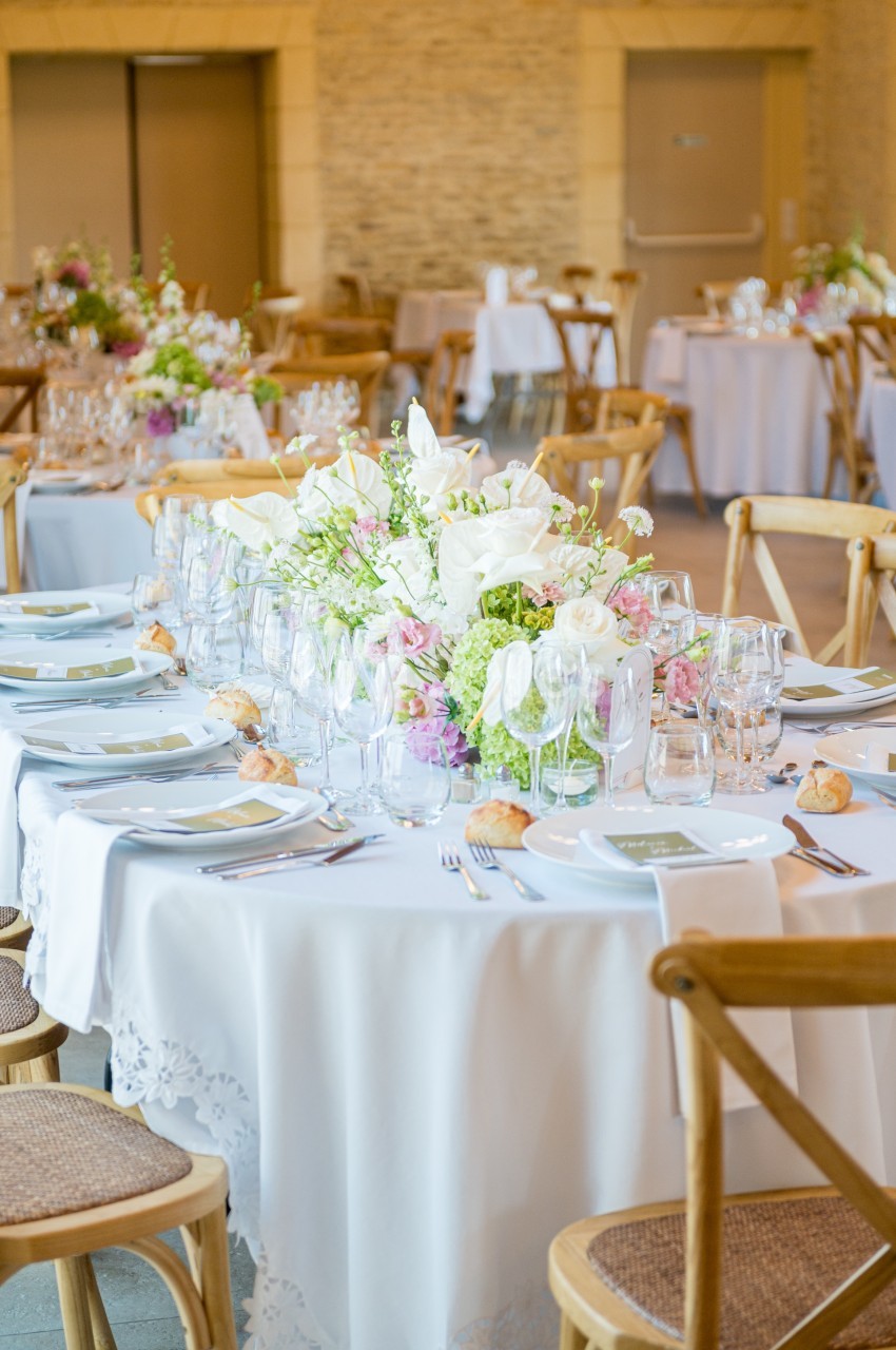 Table de réception élégamment dressée avec nappes blanches, vaisselle, verres et centre de table floral.