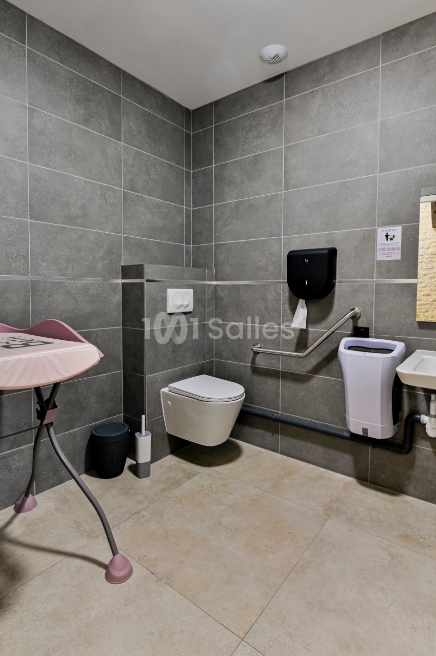 Salle de bain accessible avec toilettes suspendues, barre d'appui, table à langer et lavabo adapté.