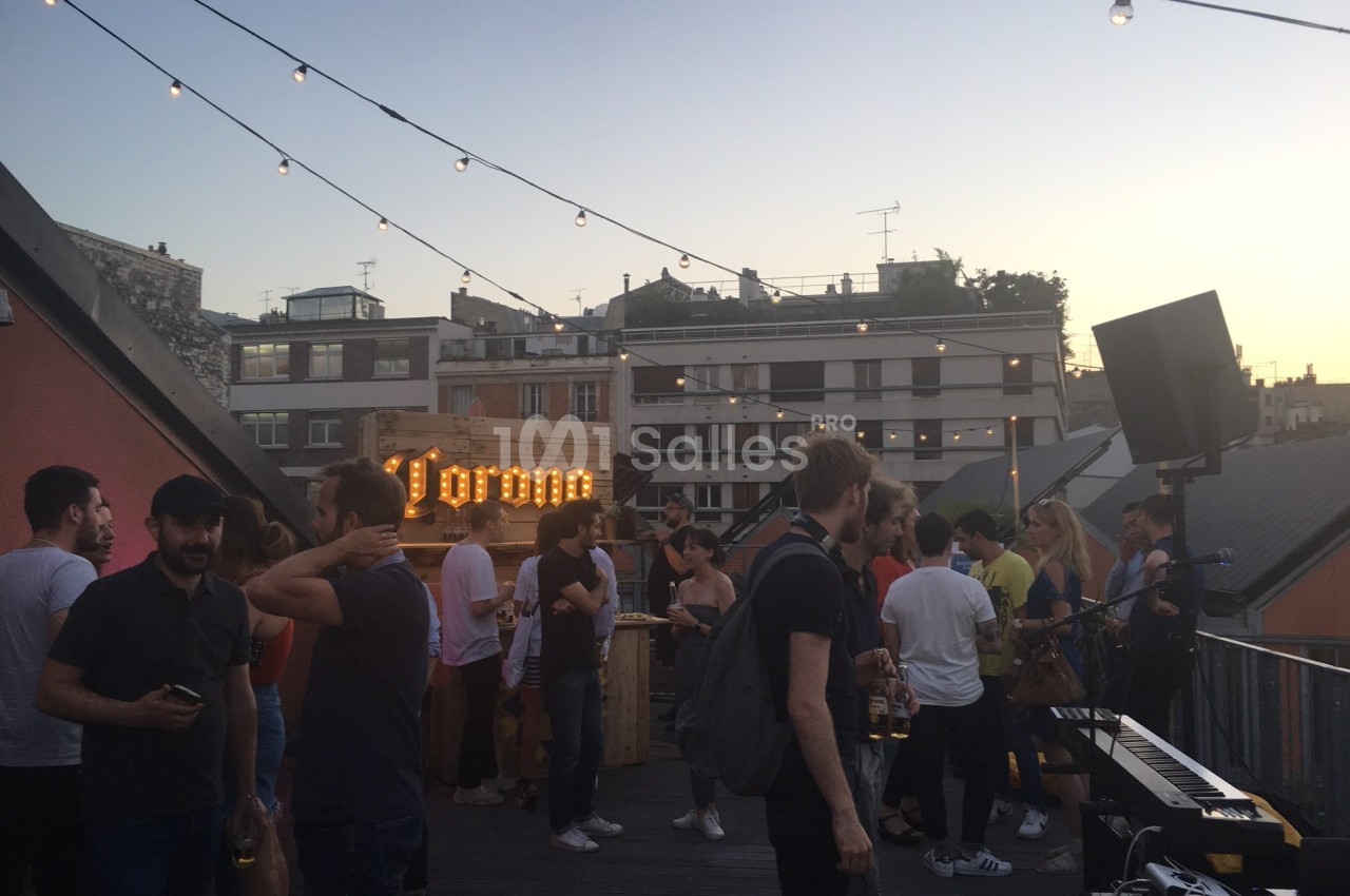 Groupe de personnes discutant et profitant d'une soirée sur une terrasse au coucher du soleil, avec des guirlandes…