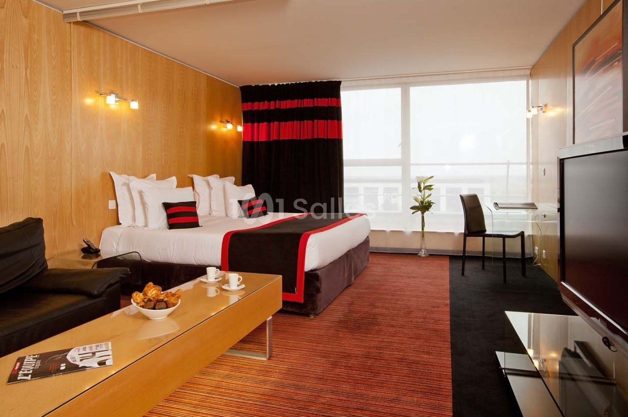 Chambre d'hôtel moderne avec lit double, bureau, canapé, table basse et grande fenêtre laissant entrer la lumière naturelle.