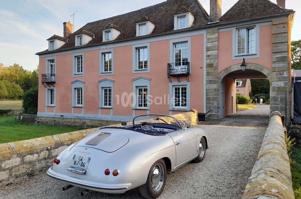 Voiture ancienne décapotable argentée stationnée devant une grande maison de style classique avec façade rose.