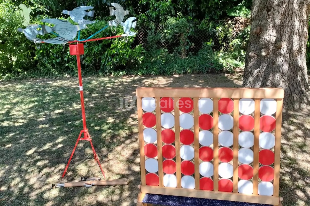Un jeu de puissance 4 géant en bois et un moulin à vent rouge installés dans un jardin ombragé.