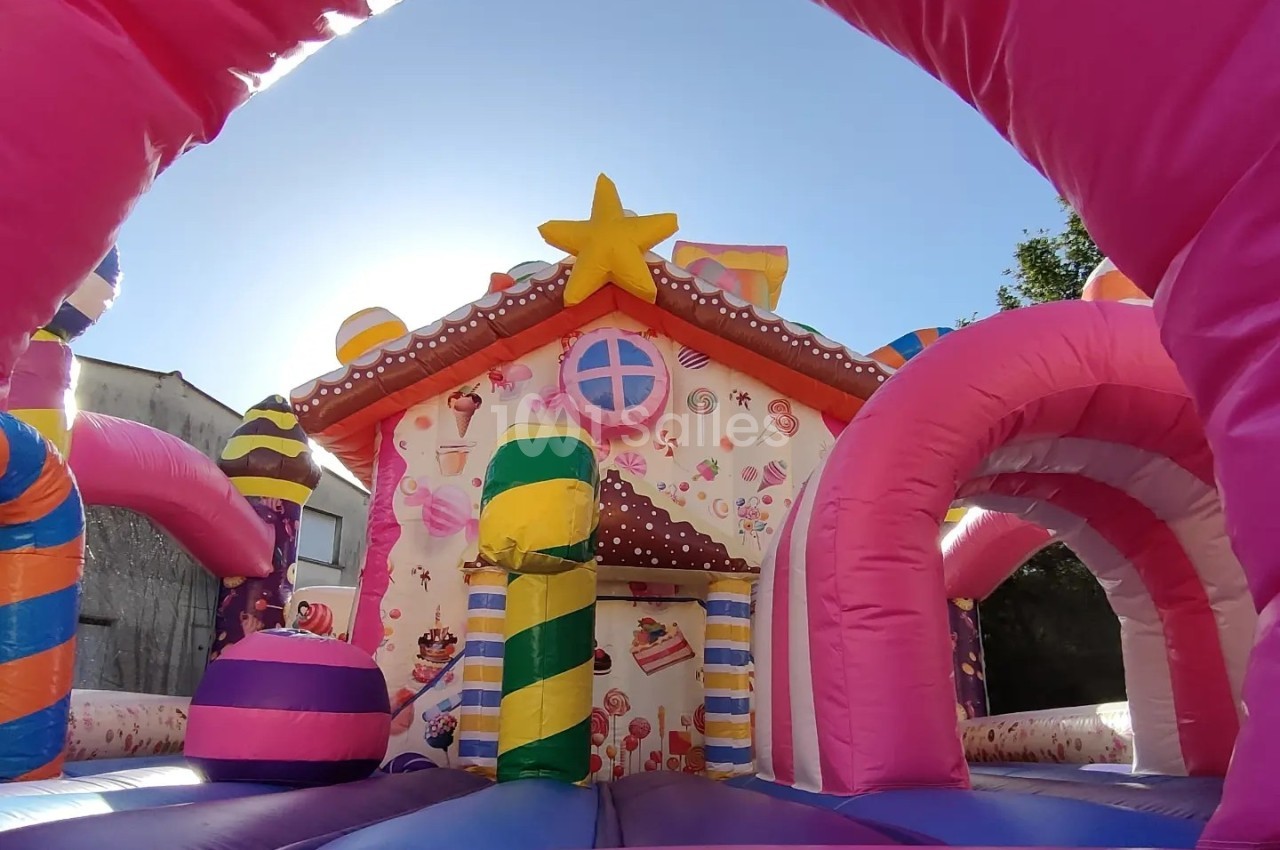 Structure gonflable colorée en forme de maison en pain d'épices avec des décorations sucrées, vue sous un ciel dégagé.