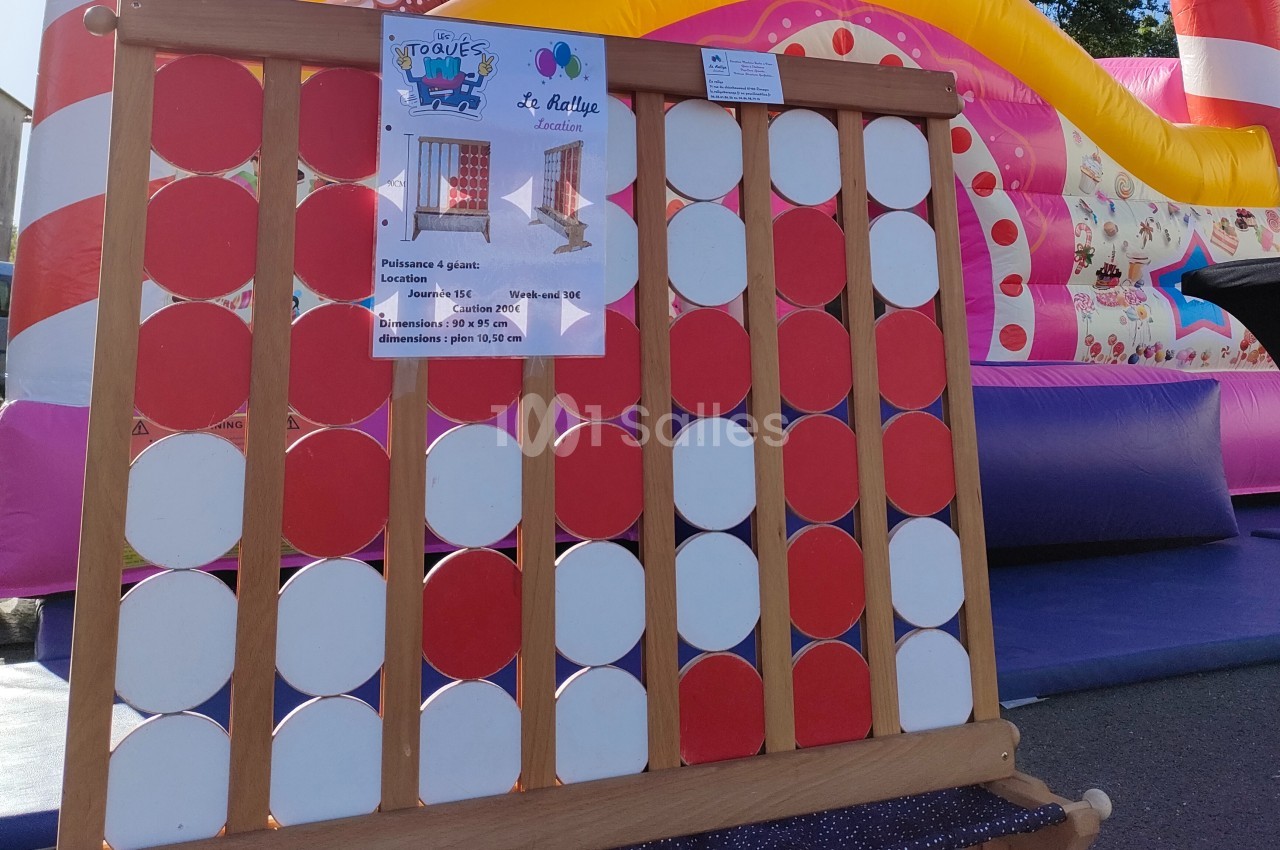 Jeu de puissance 4 géant en bois avec des pions rouges et blancs, installé devant une structure gonflable colorée.